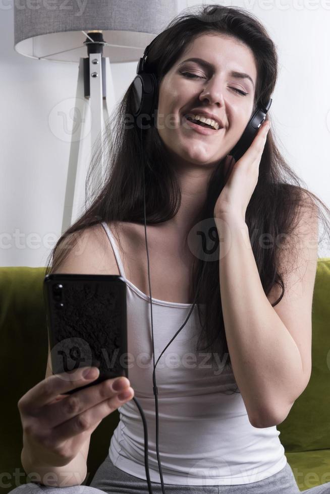 Cheerful young woman listening music in headphones in loft apartment photo