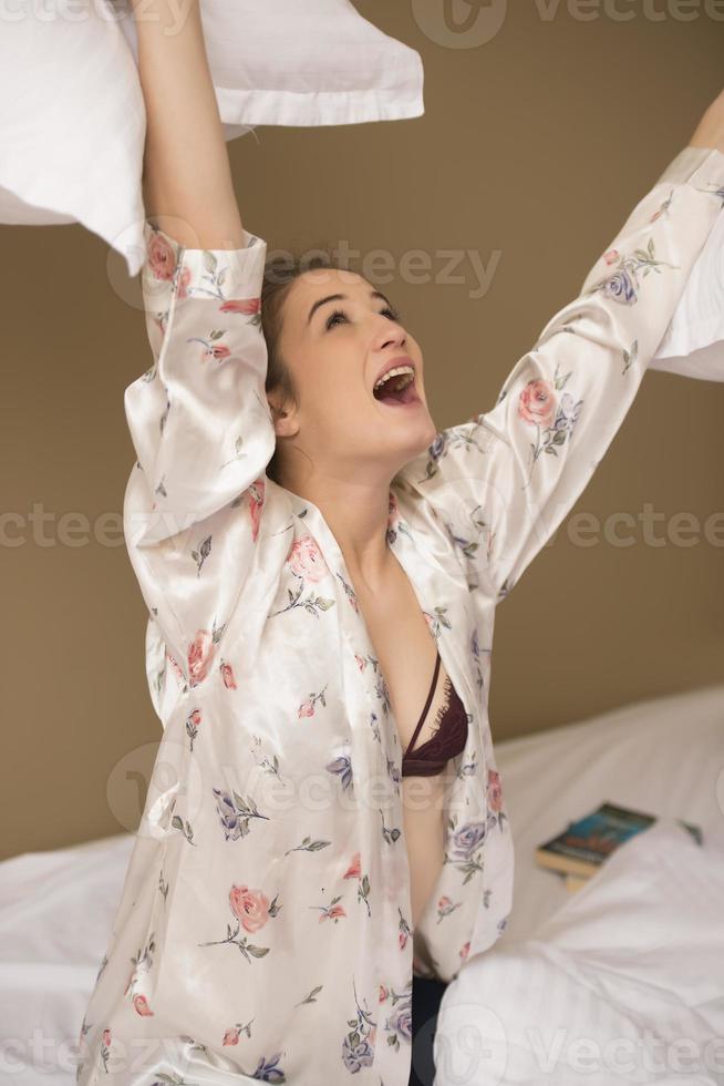 Young woman hugging pillow on comfortable bed with silky linens photo