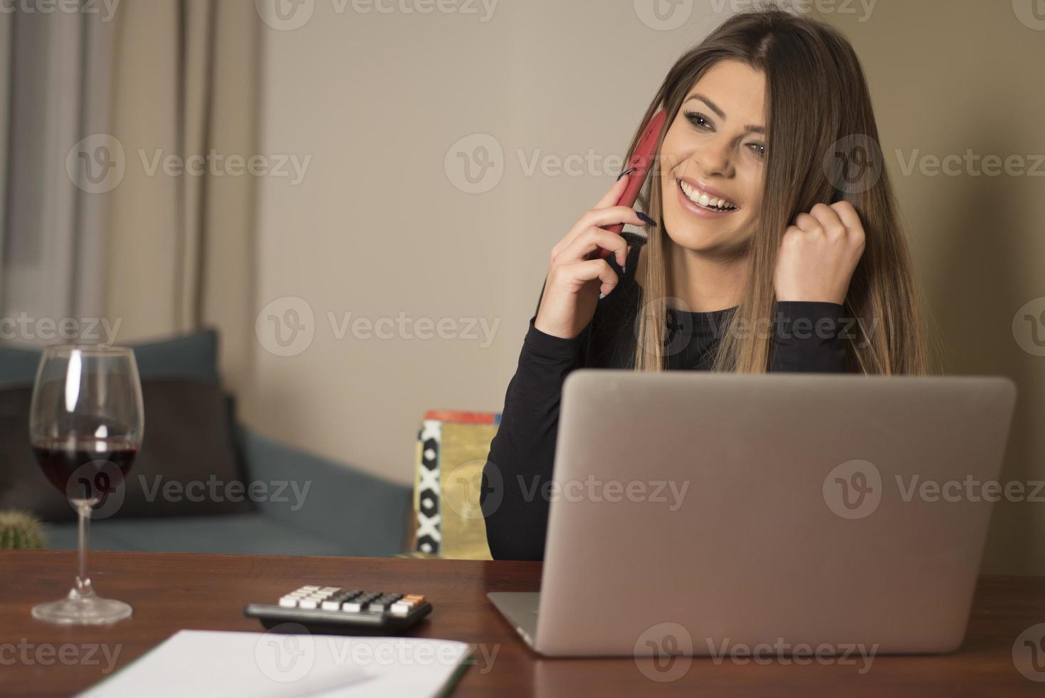 bella joven con ropa informal usando una laptop y sonriendo mientras trabaja en el interior foto