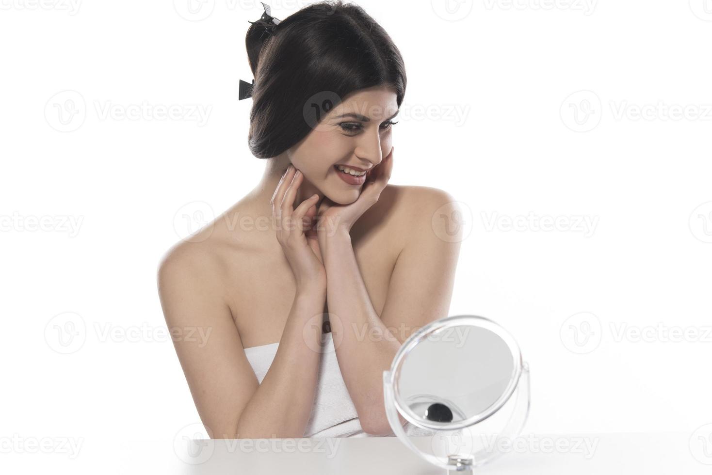 beautiful attractive brunette woman checking her face skin in front of a mirror on white background photo