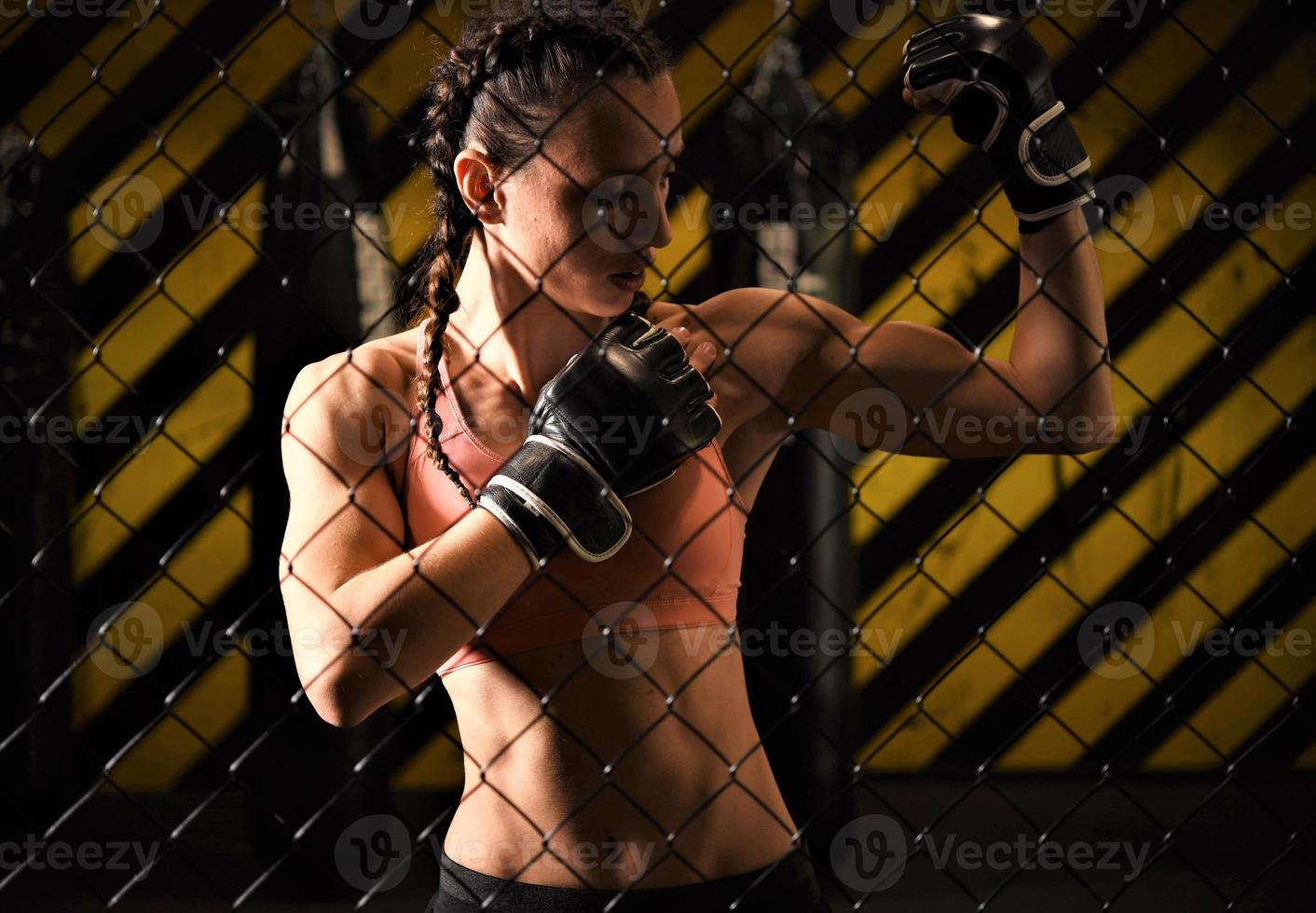 A female trainee of mixed martial arts wearing a hand wrap warms up within the ring cage by stretching her back and legs. photo
