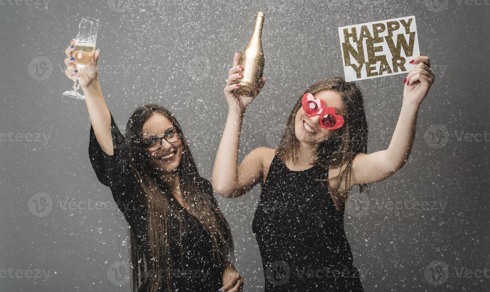 Two female friends celebrating New Year with confetti and champagne holding sign. isolated photo