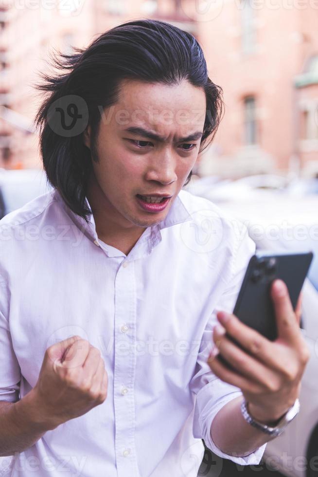 portrait of Young smiling handsome Asian man in semi formal suit using mobile phone photo
