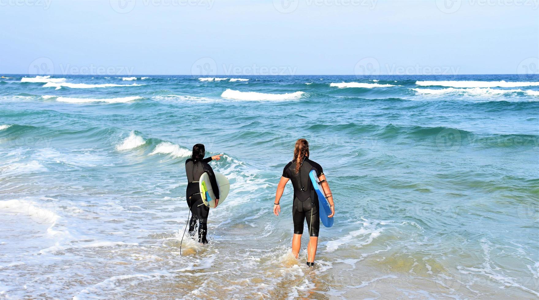Surfers couple waiting for the high waves on beach - Sporty people with surf boards on the beach - Extreme sport and vacation concept photo