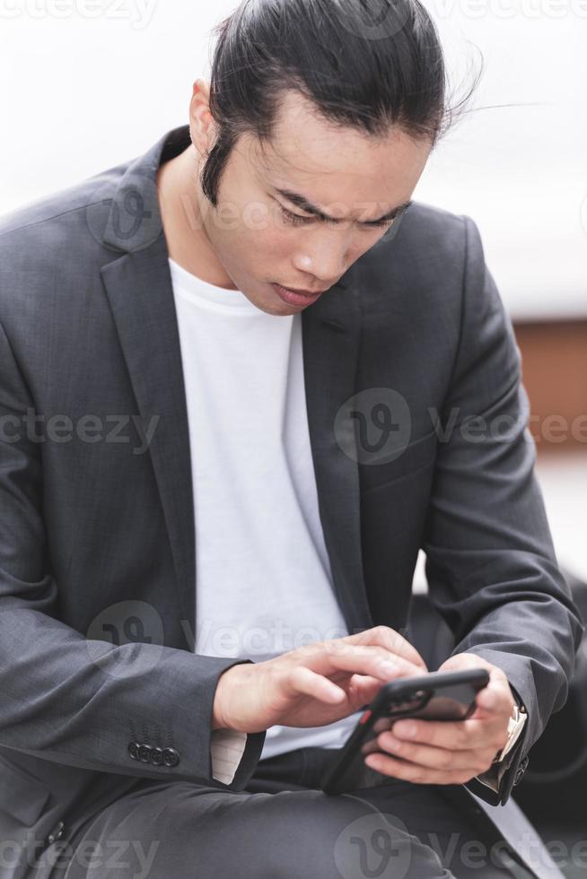 portrait of Young smiling handsome Asian man in semi formal suit using mobile phone photo