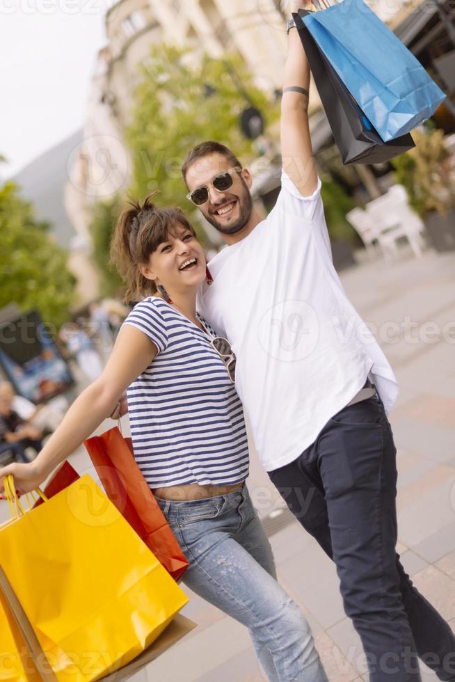 Portrait of cheerful Caucasian young couple man and woman holding many paper bags after shopping while walking and talking on street. Happy family couple with packages outdoor. Buying concept photo