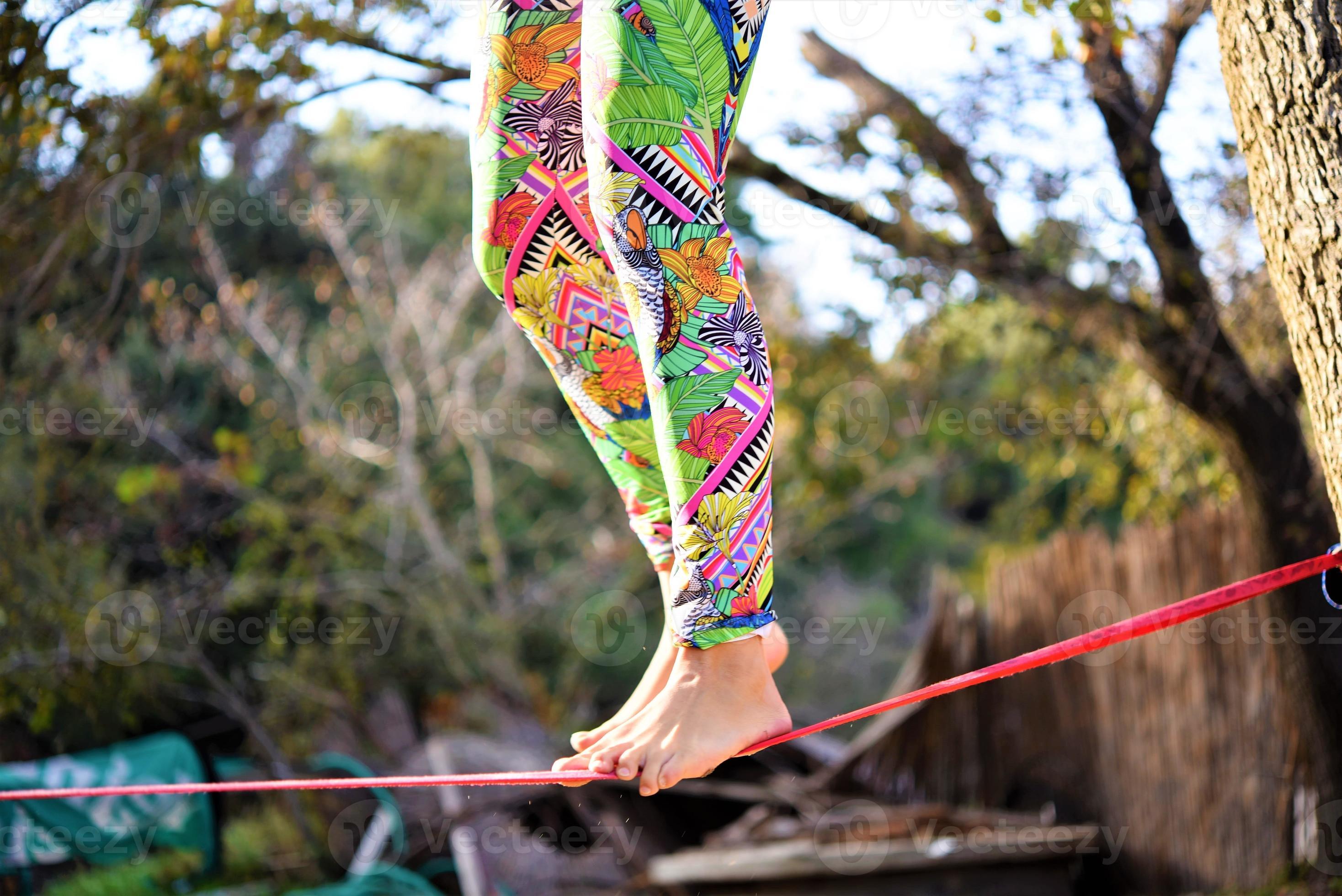 Woman balancing her walk on a loose rope tied between two trees. Woman  practicing slack rope walking in a park. 16606663 Stock Photo at Vecteezy