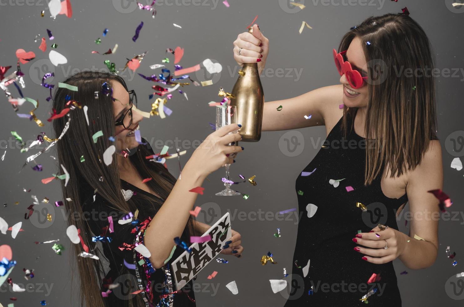 Two female friends celebrating New Year with confetti and champagne holding sign. isolated photo