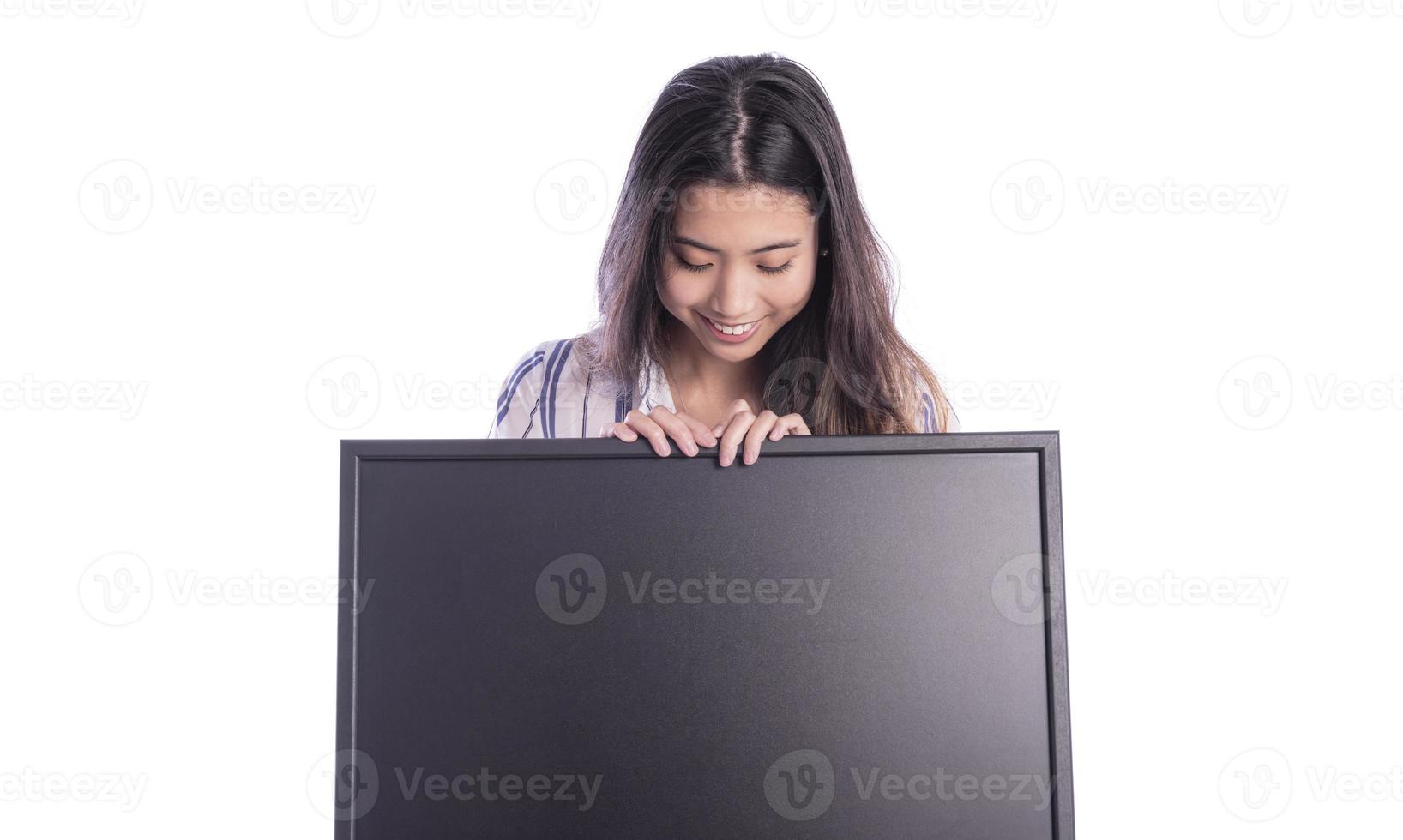 Portrait of young beautiful woman peeping at the camera holding white blank sign showing on it with finger. photo