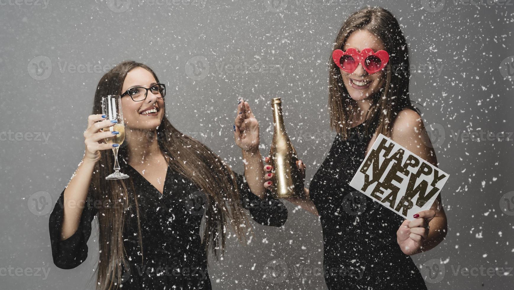 Two female friends celebrating New Year with confetti and champagne holding sign. isolated photo