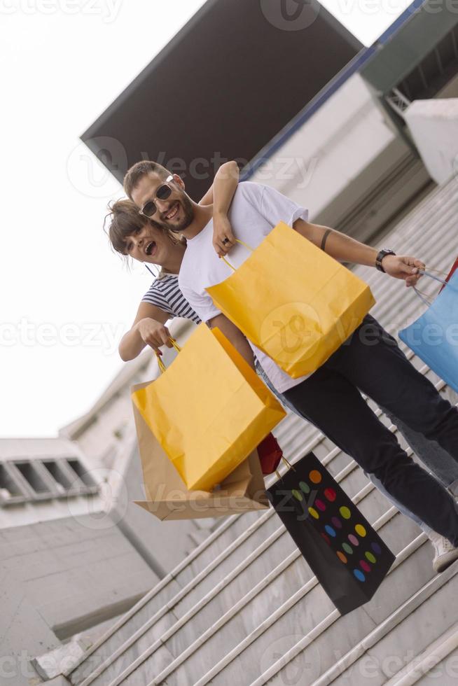 retrato de una alegre pareja joven caucásica hombre y mujer sosteniendo muchas bolsas de papel después de ir de compras mientras camina y habla en la calle. feliz pareja familiar con paquetes al aire libre. concepto de compra foto