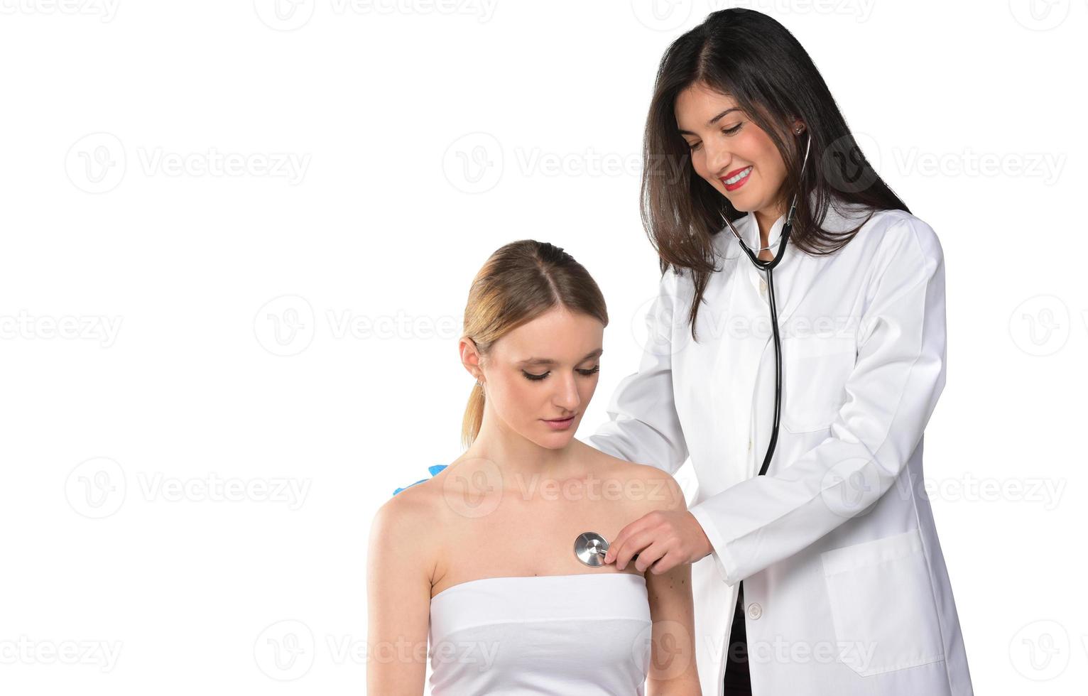una joven doctora cariñosa con mascarilla médica sostiene estetoscopio y escucha el corazón del paciente en el hospital. foto