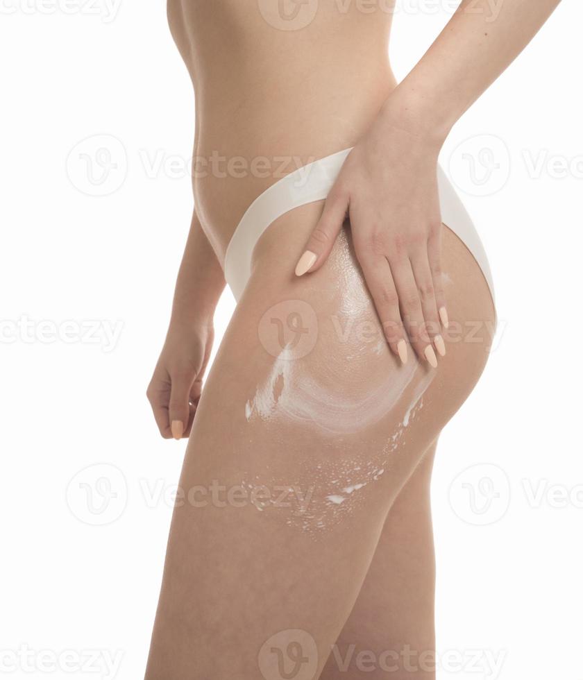 Sideways shot of slim woman applies body cream on hip photo