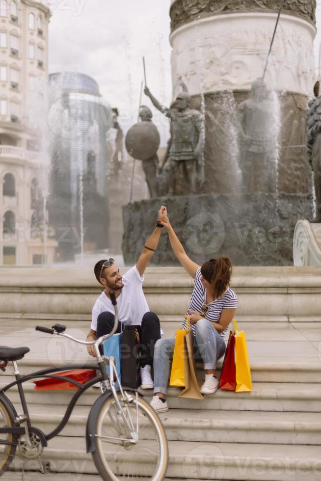 Portrait of cheerful Caucasian young couple man and woman holding many paper bags after shopping while walking and talking on street. Happy family couple with packages outdoor. Buying concept photo