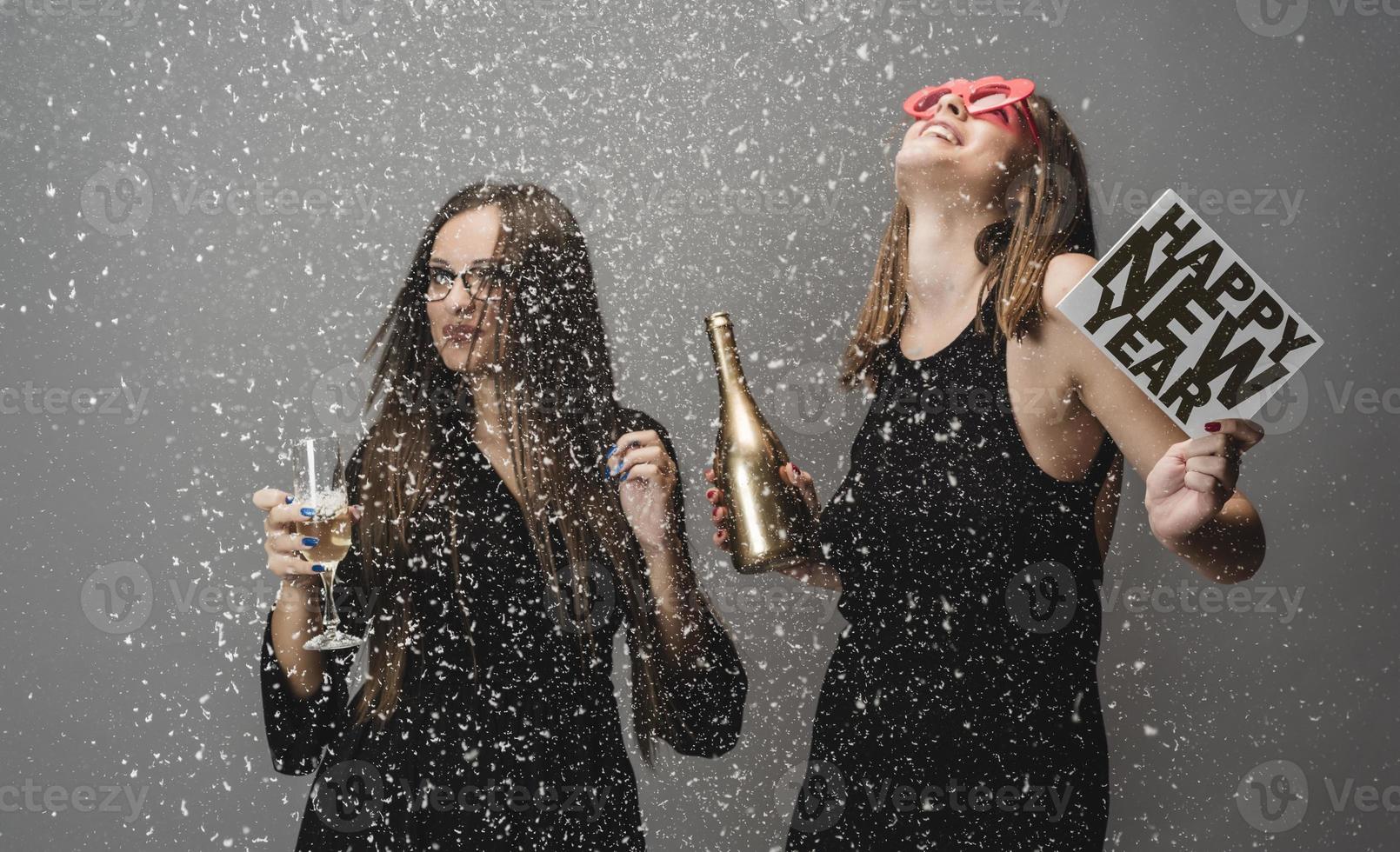 Two female friends celebrating New Year with confetti and champagne holding sign. isolated photo