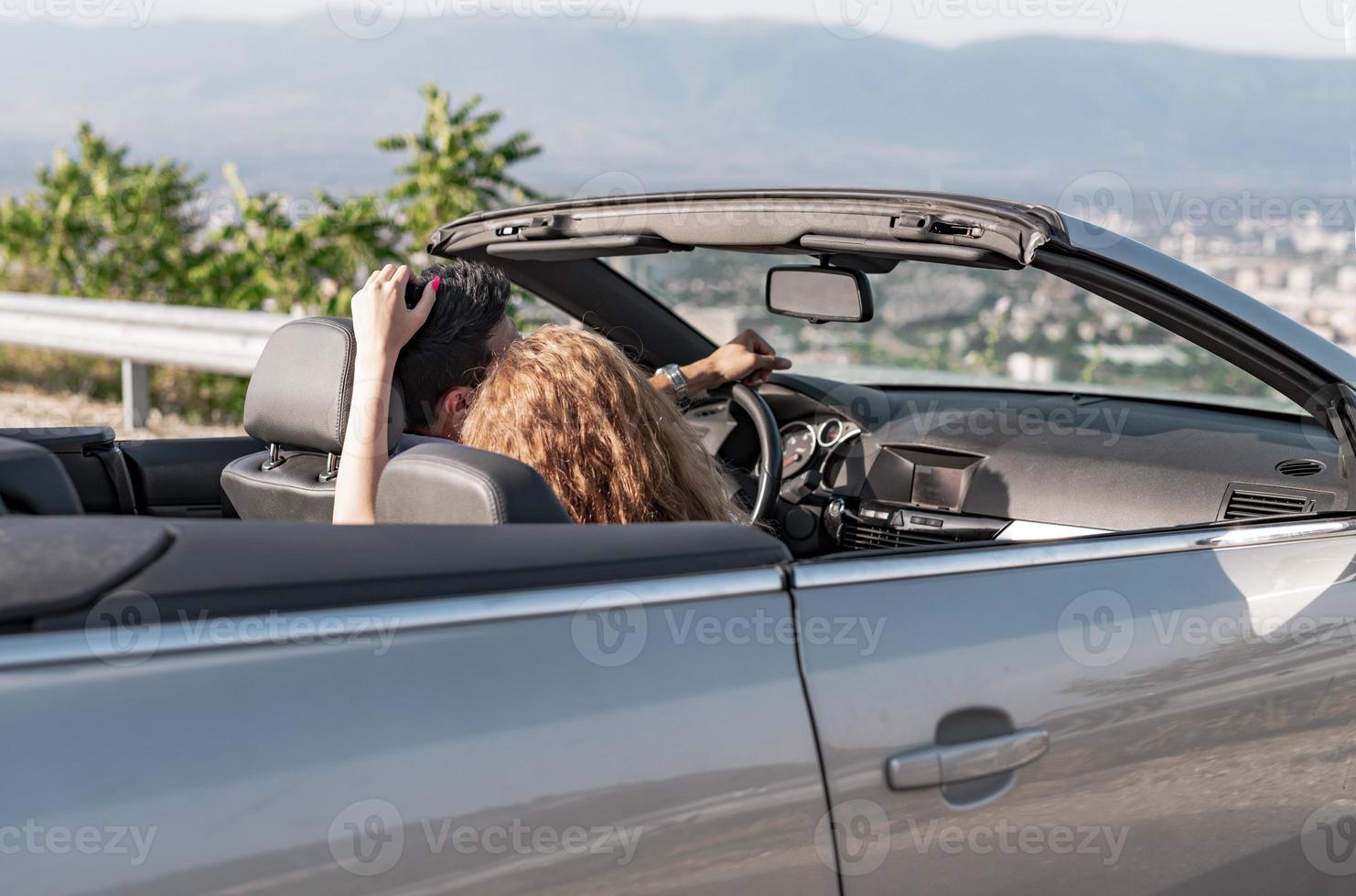 Friends having fun at car trip around the world. Couple in love with arms up on a convertible car. photo