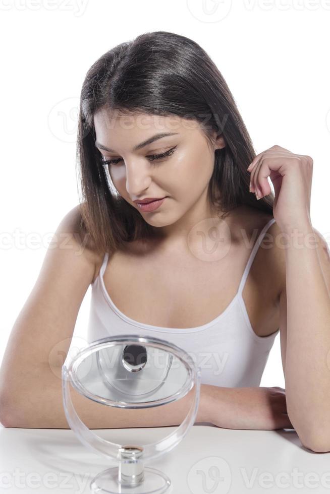 Portrait of a girl putting cosmetic ointment on face while watching at mirror indoor photo