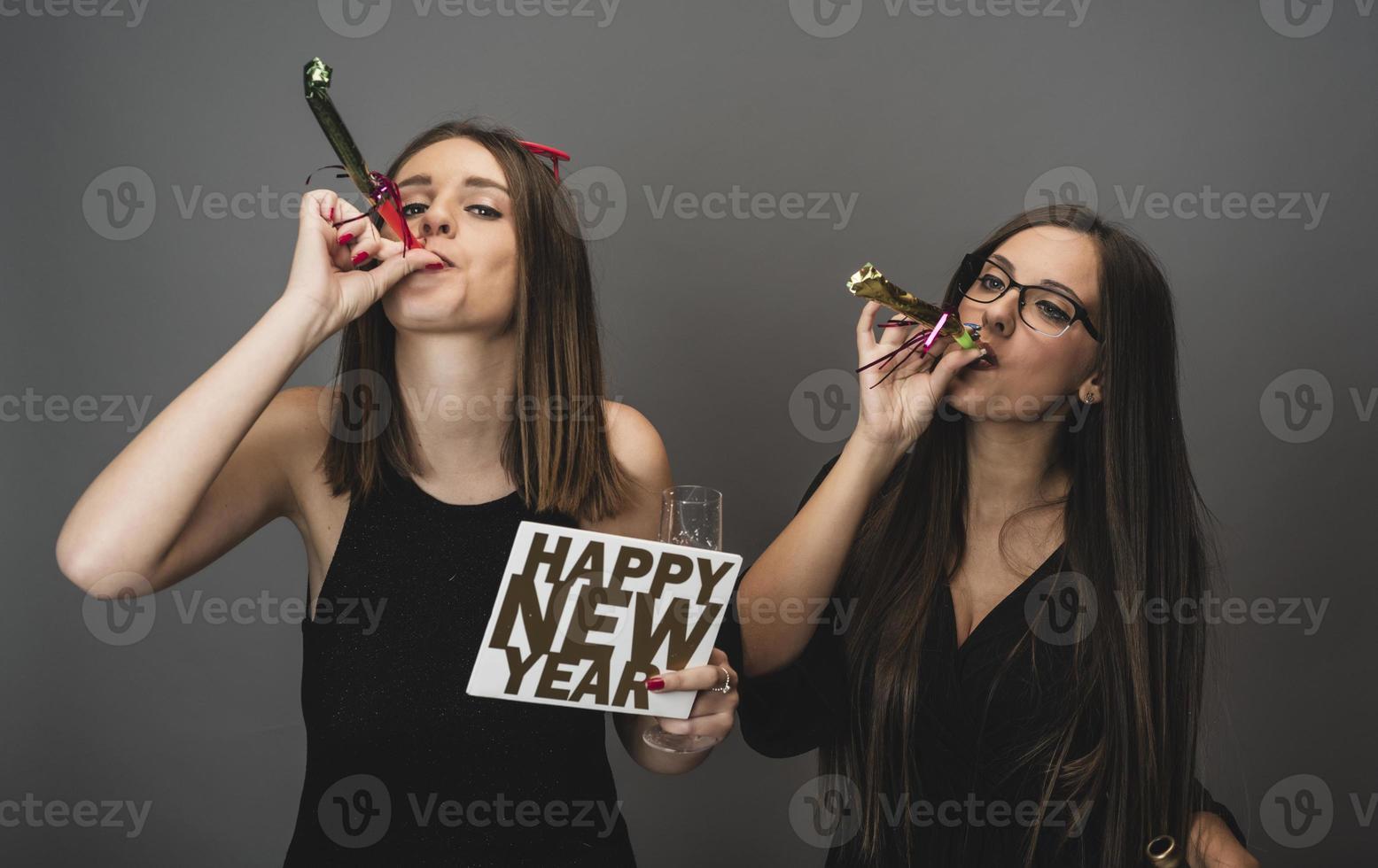 Two female friends celebrating New Year with confetti and champagne holding sign. isolated photo
