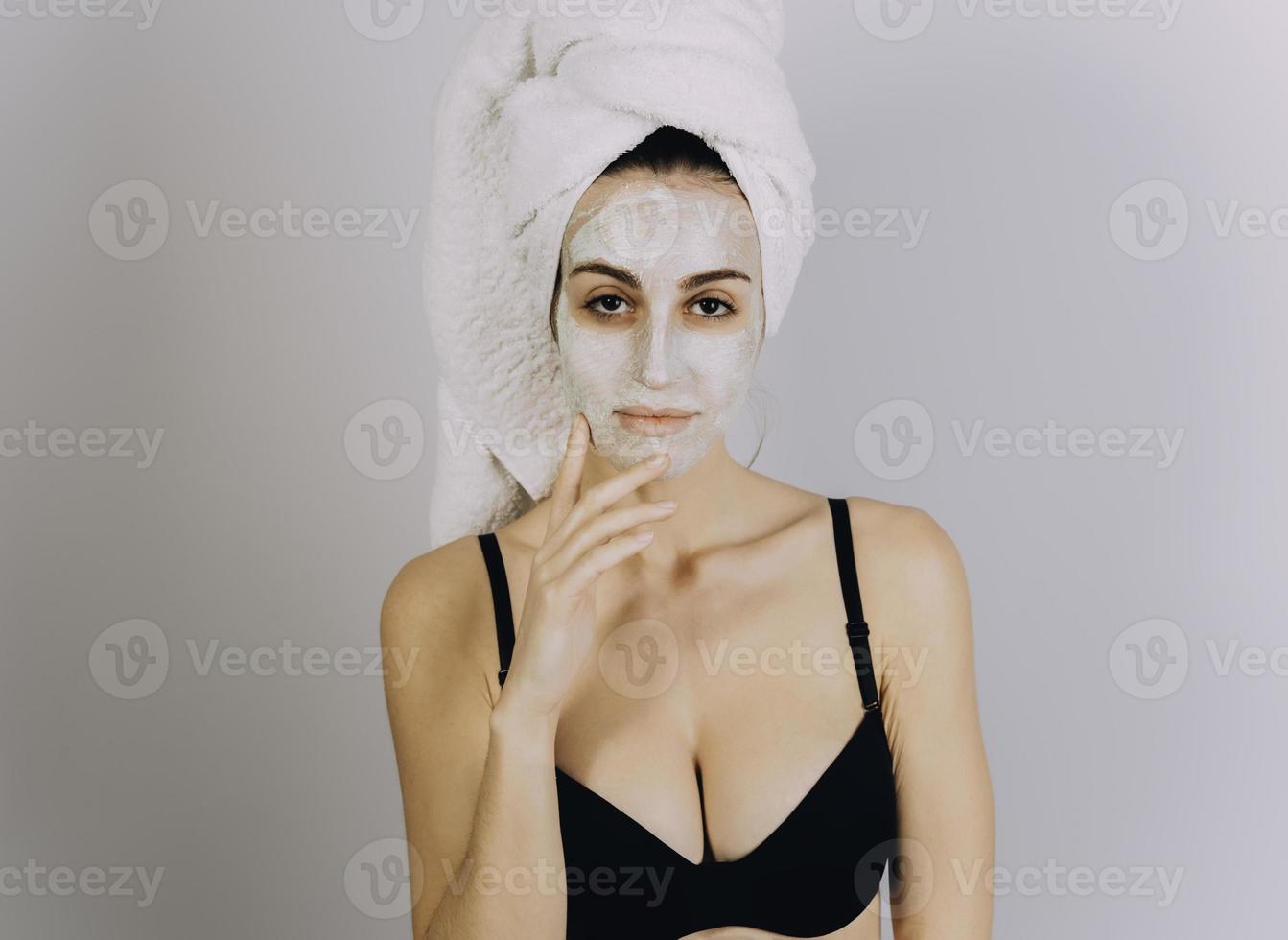 Spa Woman applying Facial clay Mask. Beauty Treatments. Close-up portrait of beautiful girl with a towel on her head applying facial mask. photo