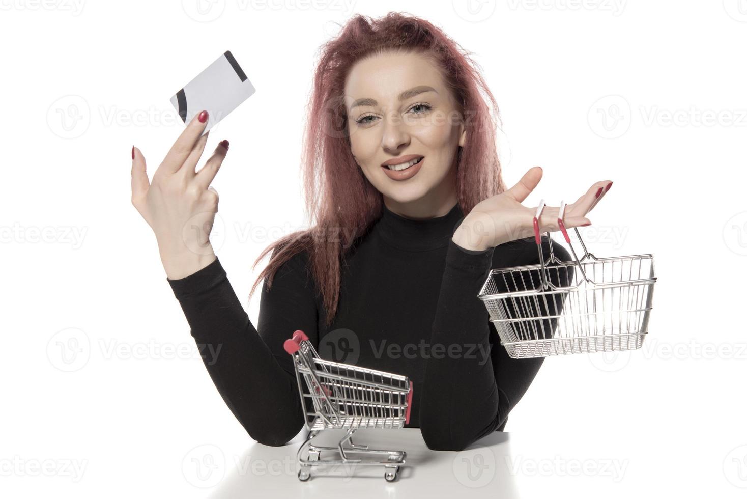 hembra feliz sosteniendo tarjetas de crédito y un pequeño carrito de compras vacío aislado de fondo blanco foto