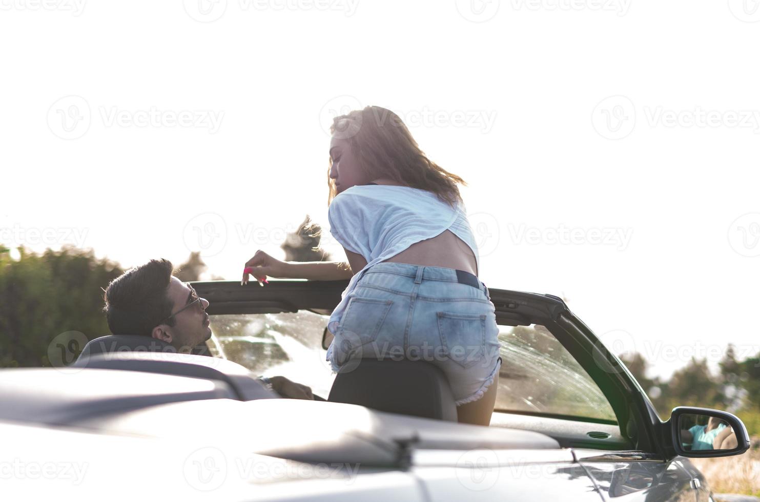 Friends having fun at car trip around the world. Couple in love with arms up on a convertible car. photo