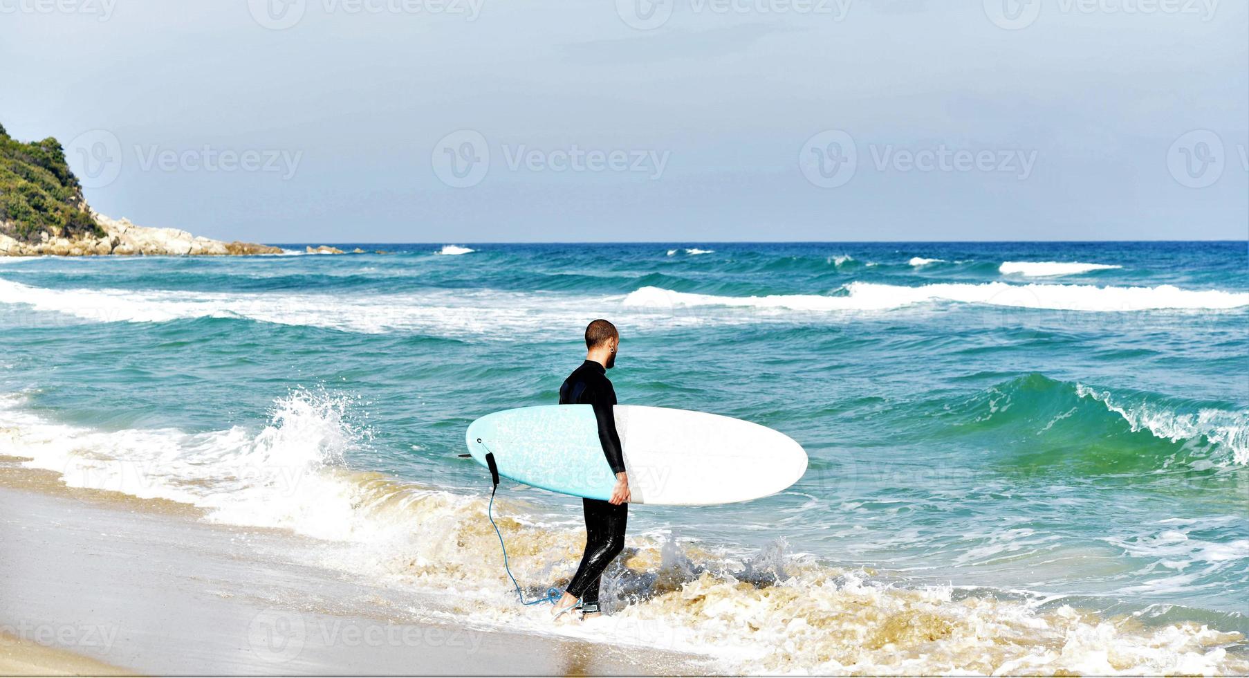 A man is standing with a surf in his hands on the sea shore. photo