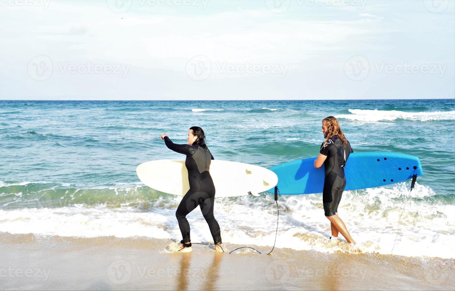 Surfers couple waiting for the high waves on beach - Sporty people with surf boards on the beach - Extreme sport and vacation concept photo
