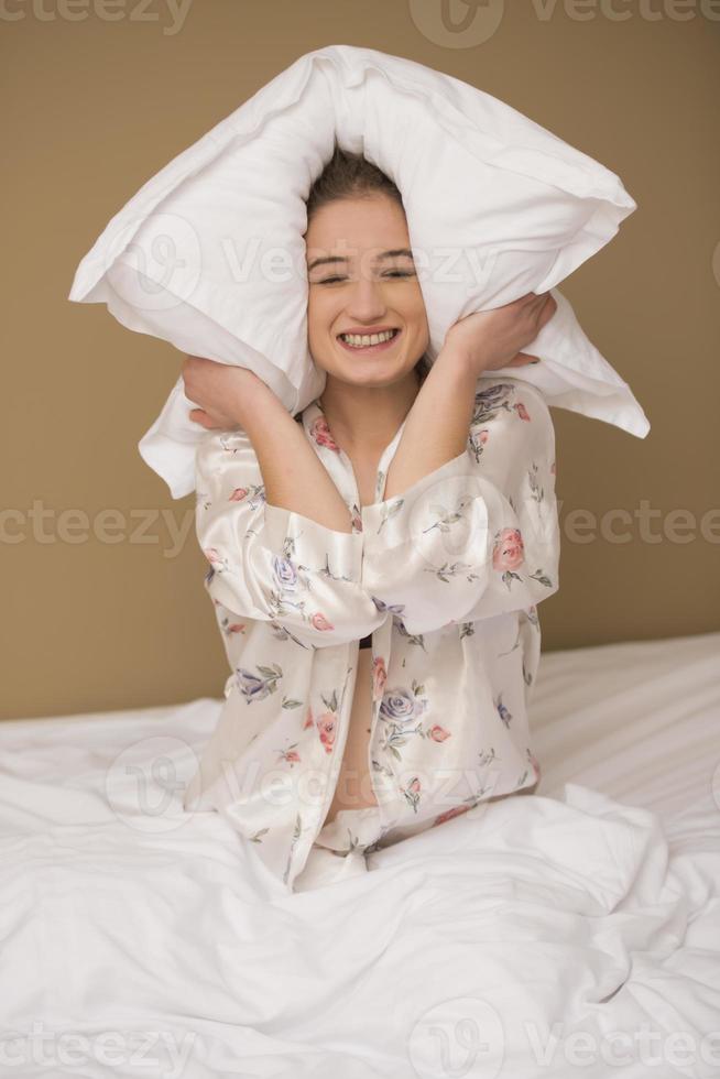 Young woman hugging pillow on comfortable bed with silky linens photo