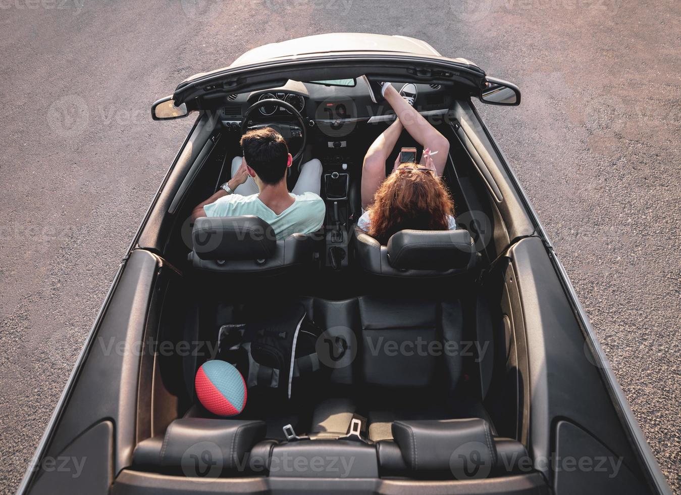 Friends having fun at car trip around the world. Couple in love with arms up on a convertible car. photo