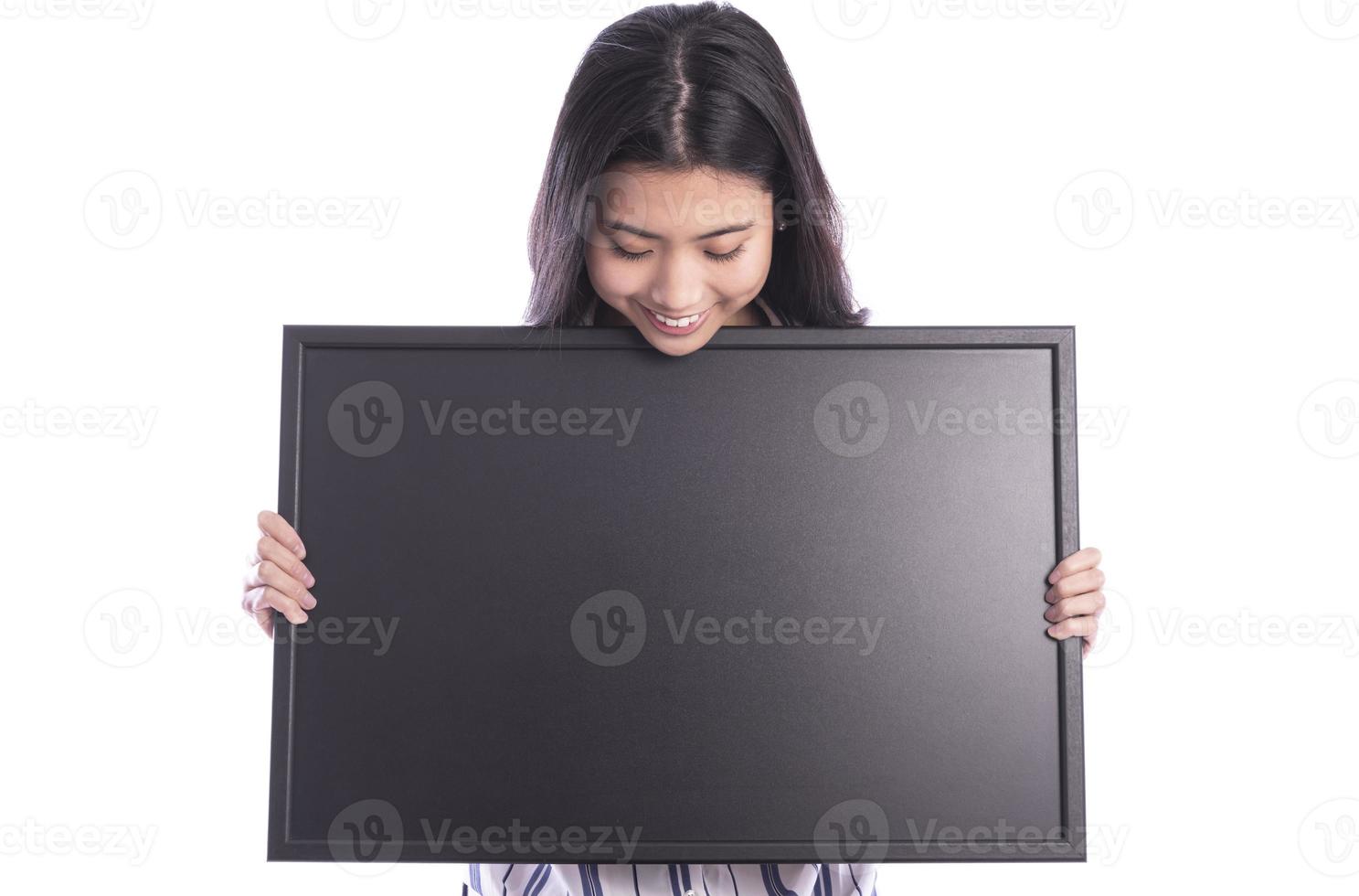 Portrait of young beautiful woman peeping at the camera holding white blank sign showing on it with finger. photo