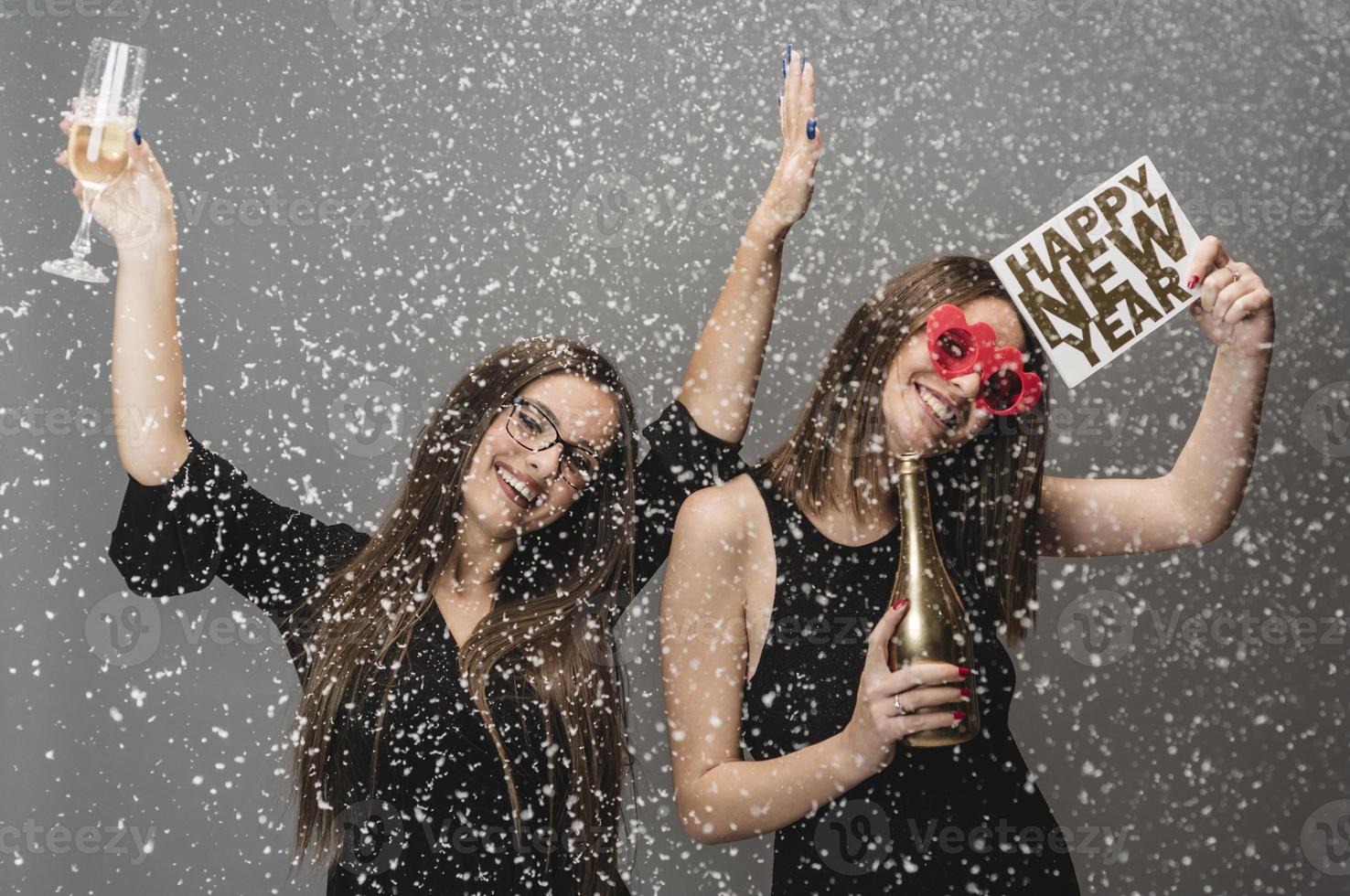 Two female friends celebrating New Year with confetti and champagne holding sign. isolated photo