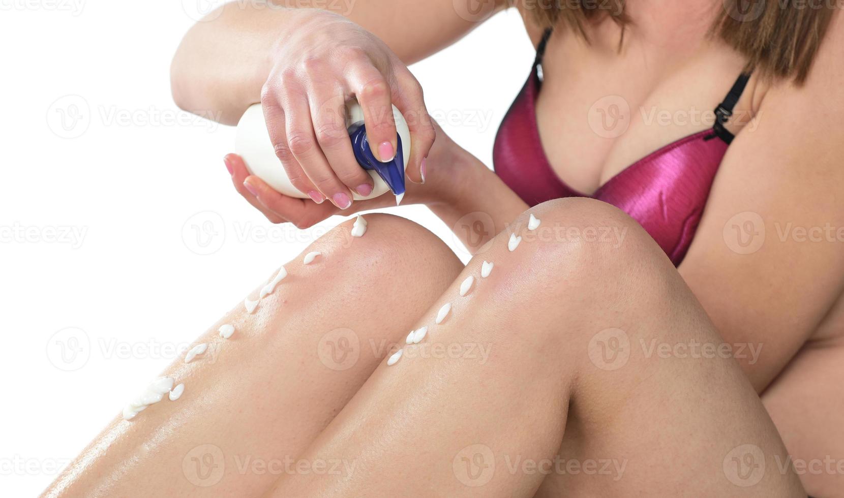 girl squeeze a bottle of body lotion to her legs photo