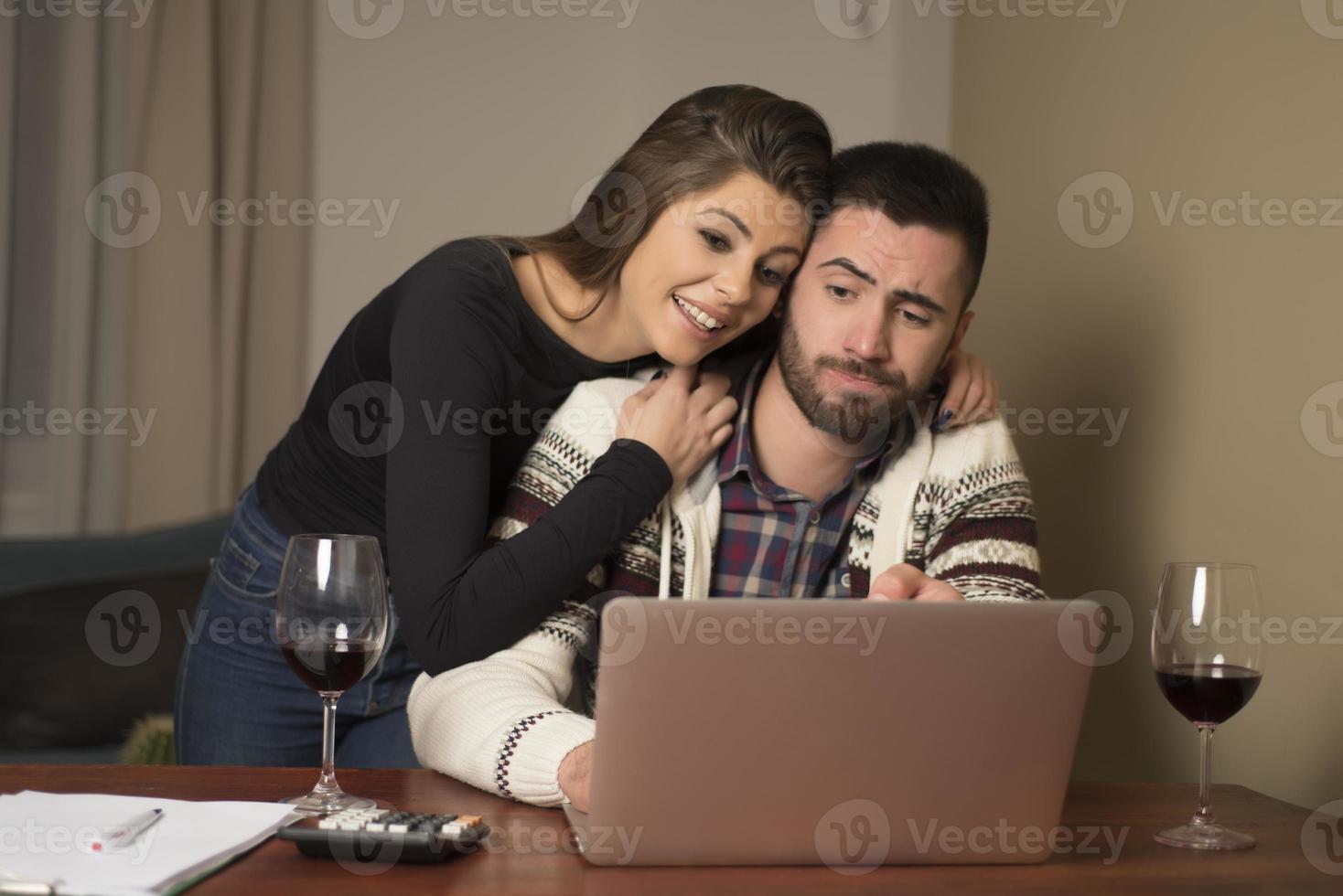 Young couple managing finances, reviewing their bank accounts using laptop computer. Woman and man doing paperwork together, paying taxes online on notebook pc photo