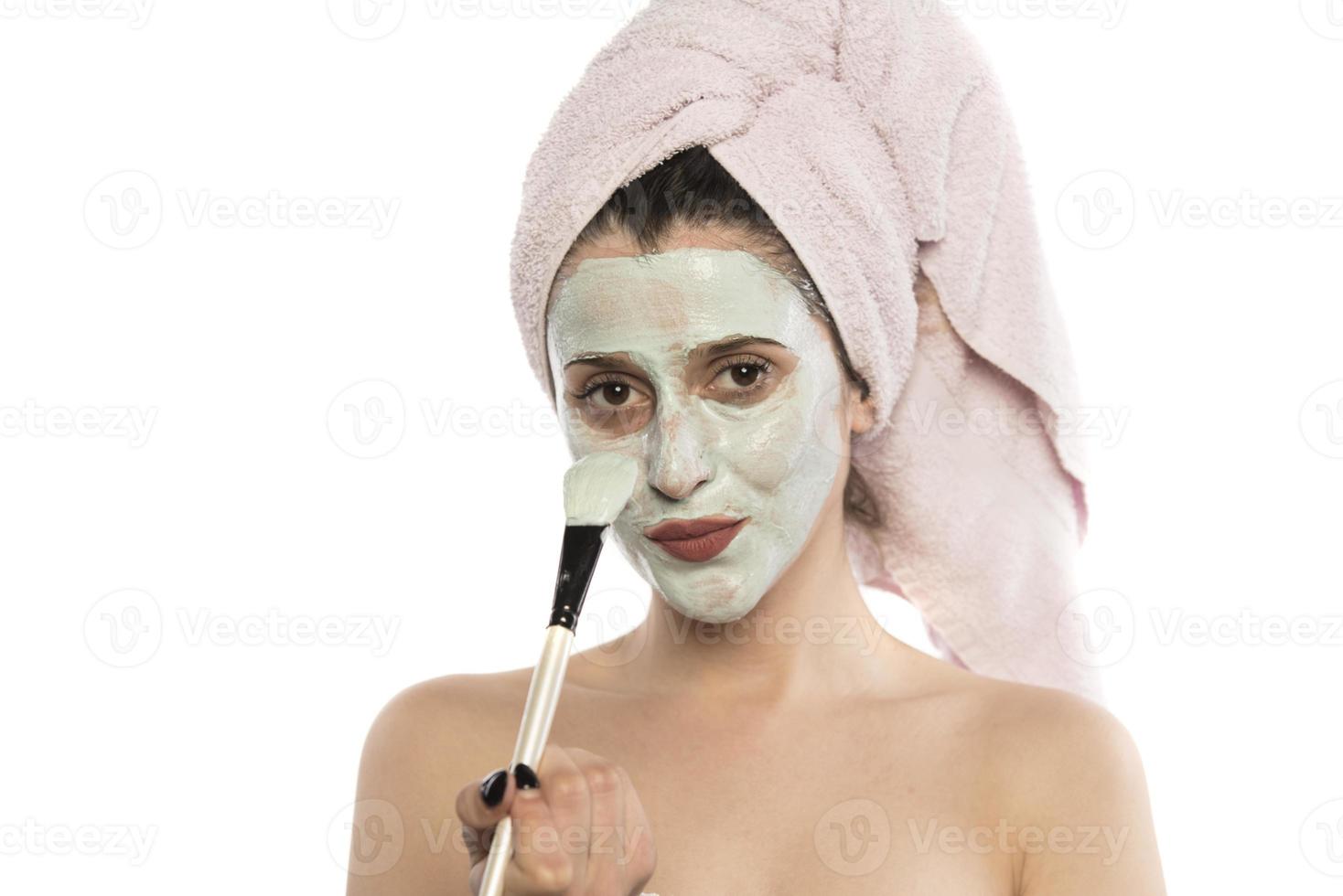 Beautiful woman having clay facial mask apply by beautician. photo