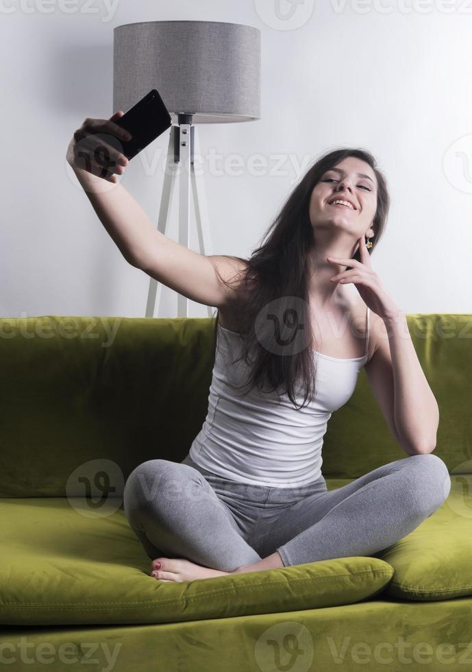 Happy woman listening to music from mobile phone while sitting on the rug beside to the sofa at homes, Smiling girl relaxing with headphones in morning, Time to relax. photo