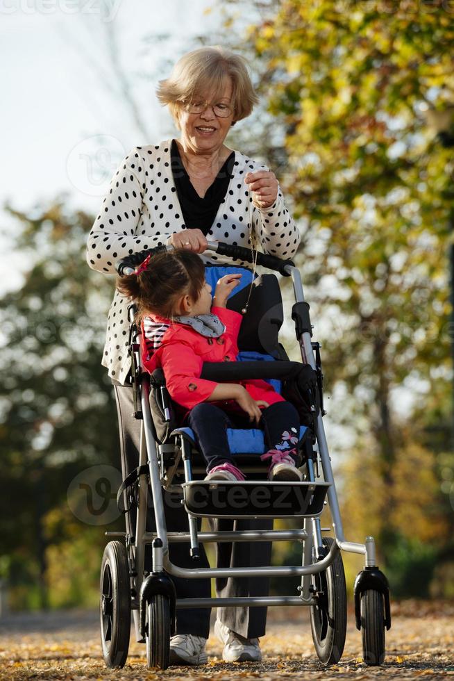 Grandmother and her autistic grand daughter enjoying holiday together outdoors, lying on green grass on blanket and smiling to camera. Leisure family lifestyle, happiness and moments. photo