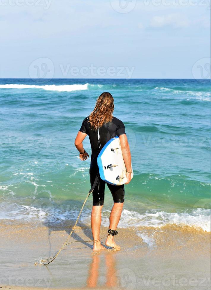 A man is standing with a surf in his hands on the sea shore. photo