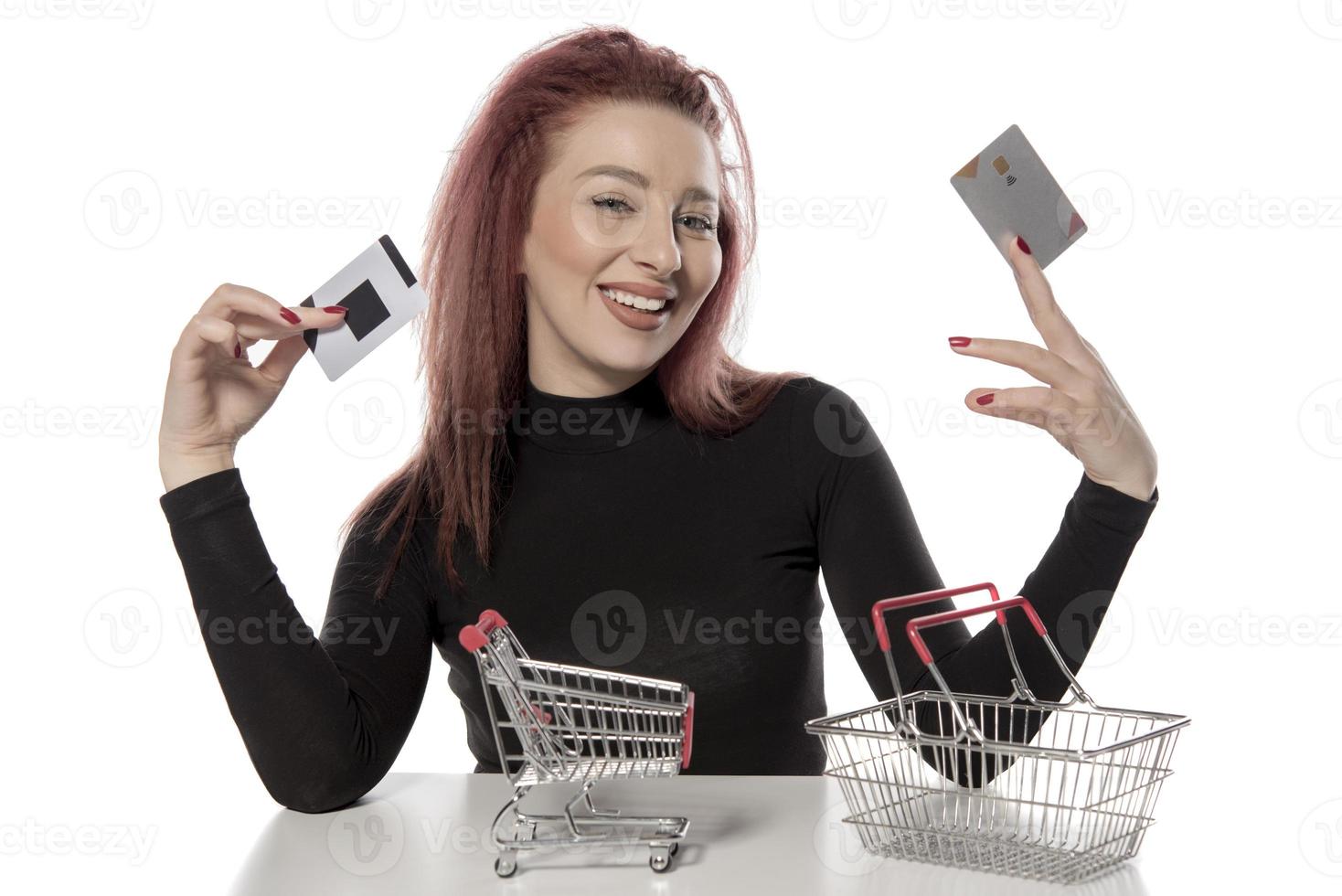 Happy female holding credit cards and a small empty shopping cart isolated on white background photo