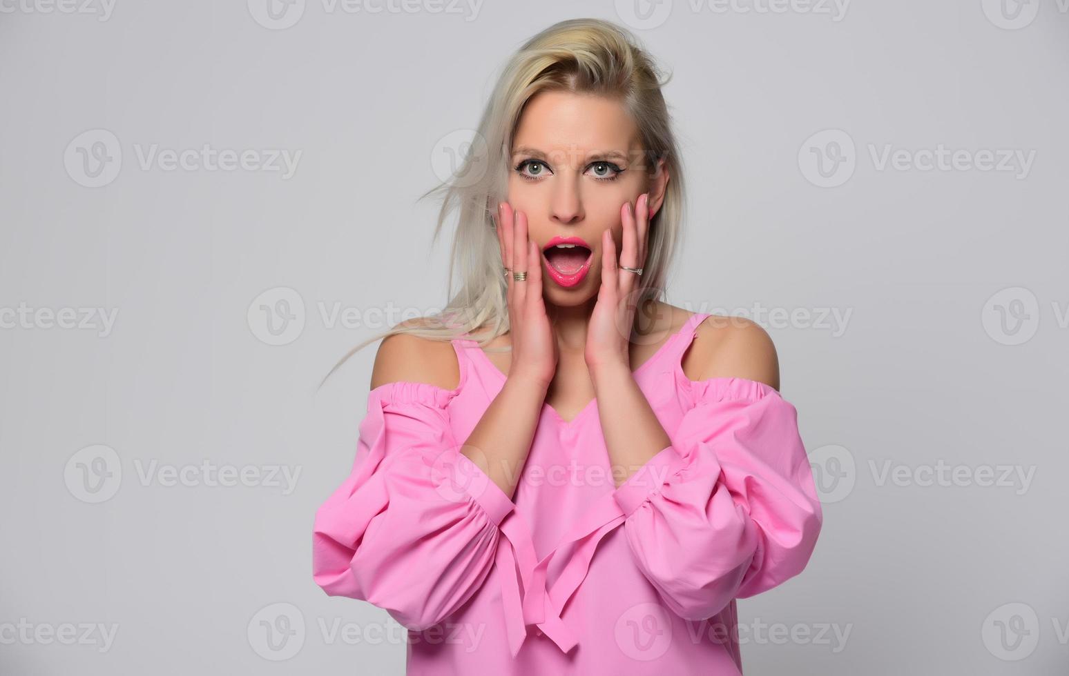 Portrait of beautiful young woman in cute pink shirt and blue jeans posing in studio. Concept of beauty, emotions, facial expression, lifestyle, fashion, youth culture photo