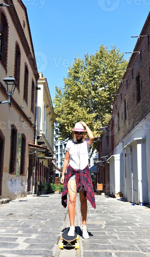 Beautiful hipster girl with skate board wearing sunglasses in the city. photo