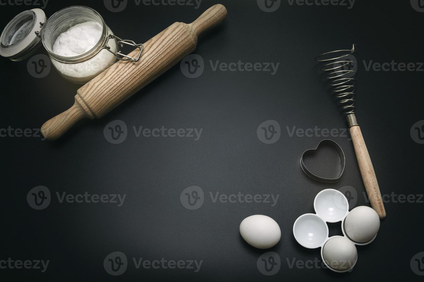 Bakery background. Baking ingredients and kitchen utensils on the black background. Top view, copy space. Modern cooking composition. Free space for text. photo