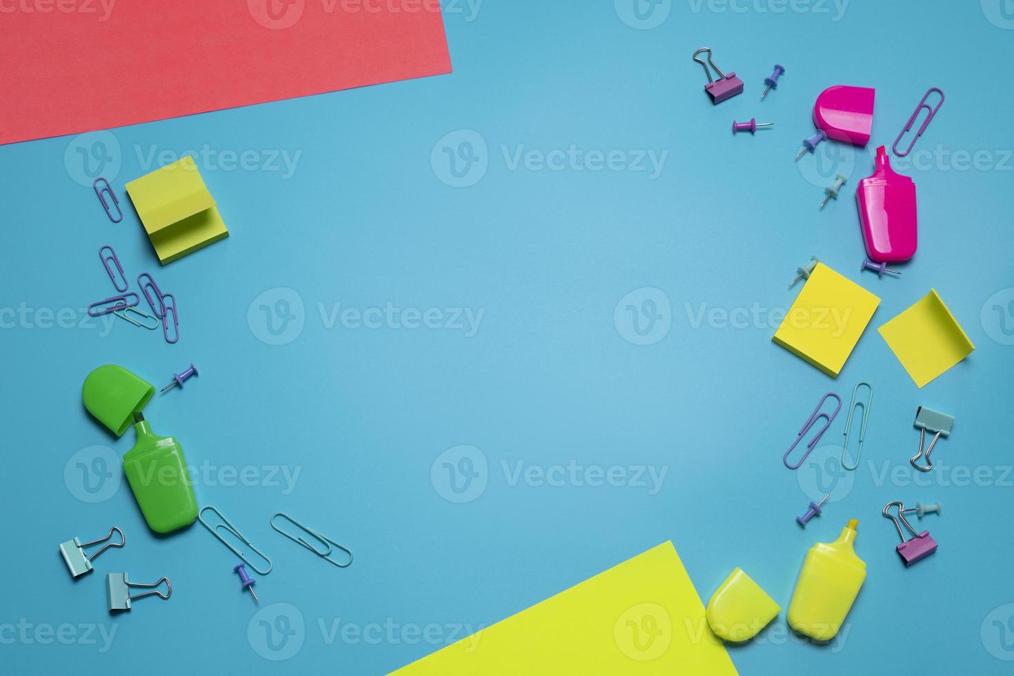 Stationery items on the blue background with free space for text. Creative, colorful background with scool or office supplies. Flatlay with copy space, top view. Markers, paper clips, sticky notes. photo