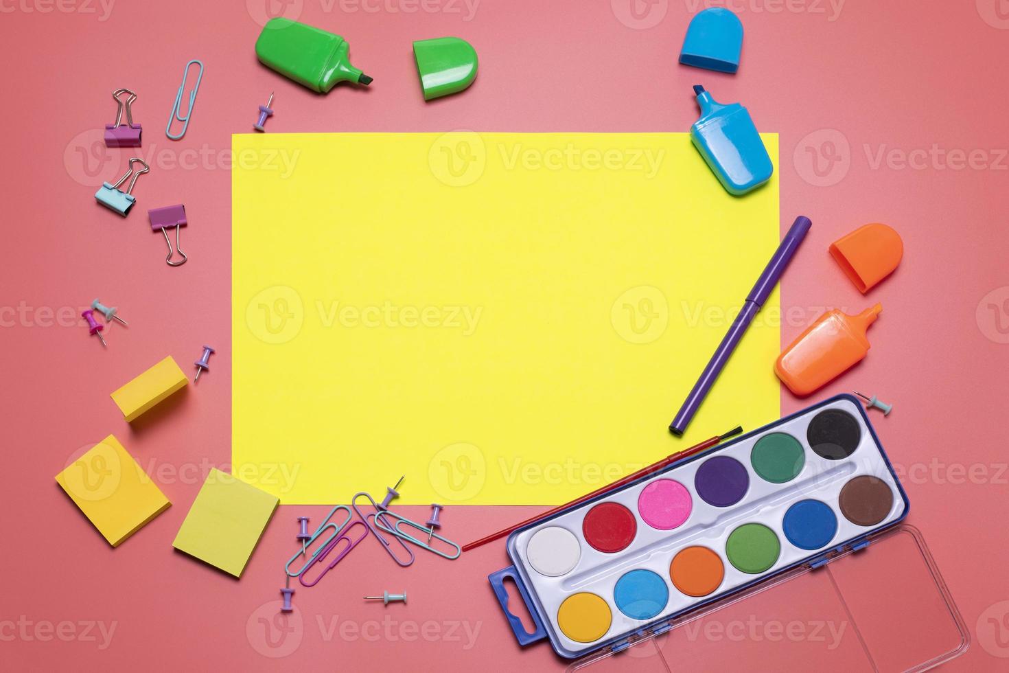 Stationery items on the pink background with free space for text. Creative, colorful background with scool supplies. Flatlay with copy space, top view. Markers, paper clips, sticky notes, yellow paper photo