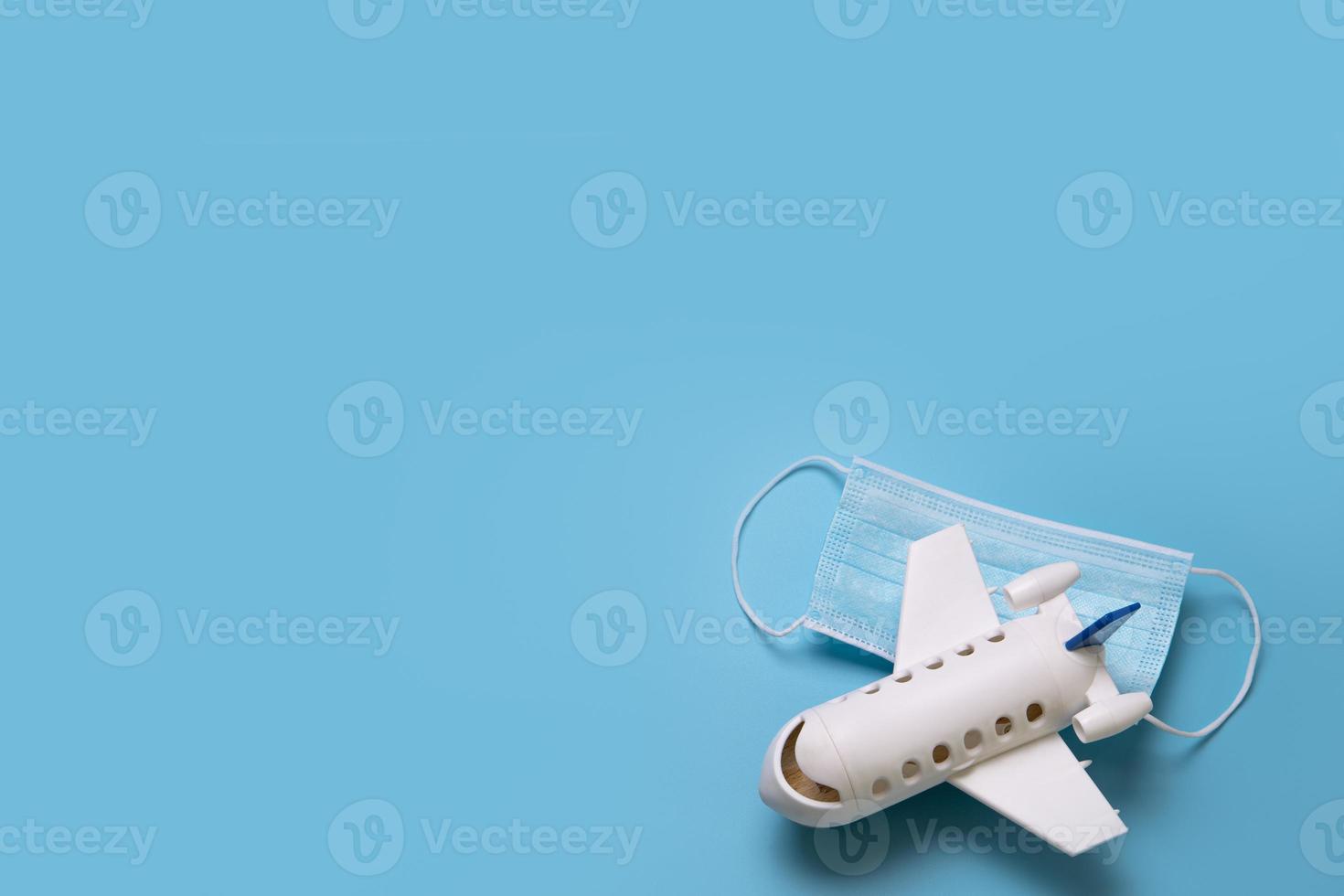 Travel during the time of COVID-19. Medical mask and mini airplane on the blue background. Free space for text. Vacation, holidays, flight in corona times. photo