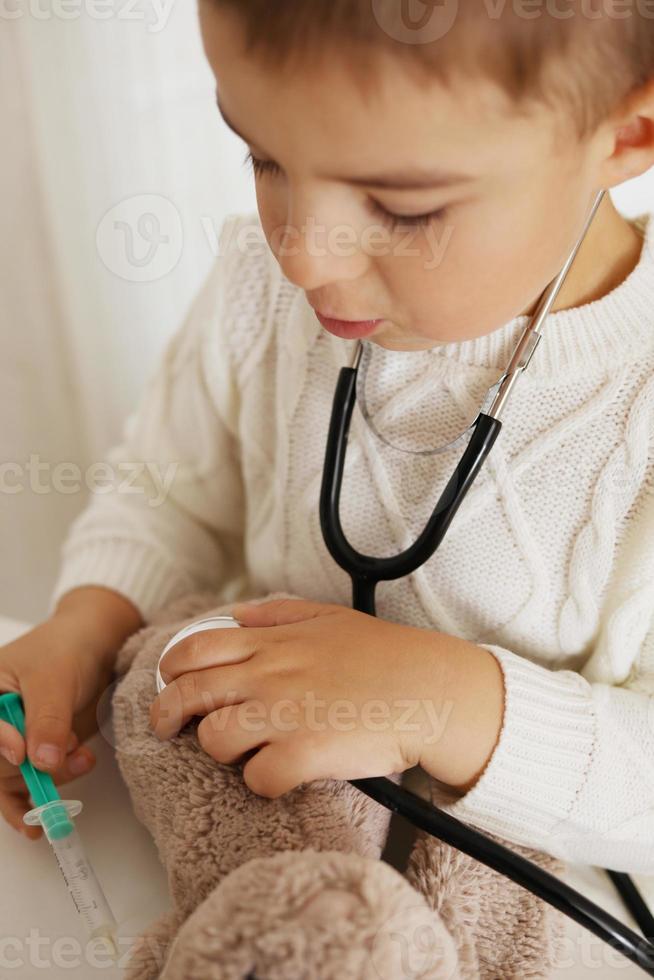 Cute little boy playing doctor at home and curing plush toy. Sweet toddler child using stethoscope. Having fun. Kids and medicine, healthcare. photo