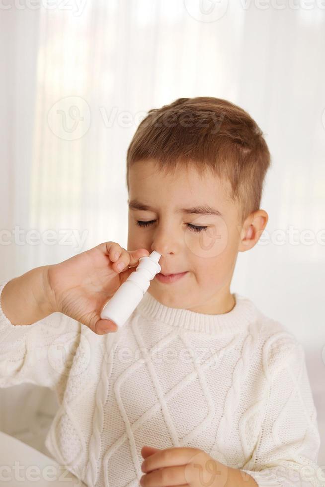 Little boy spraying medicine in nose, nose drops. Toddler child using nasal spray. Runny nose, cold, flu, illness, virus. Close up. photo