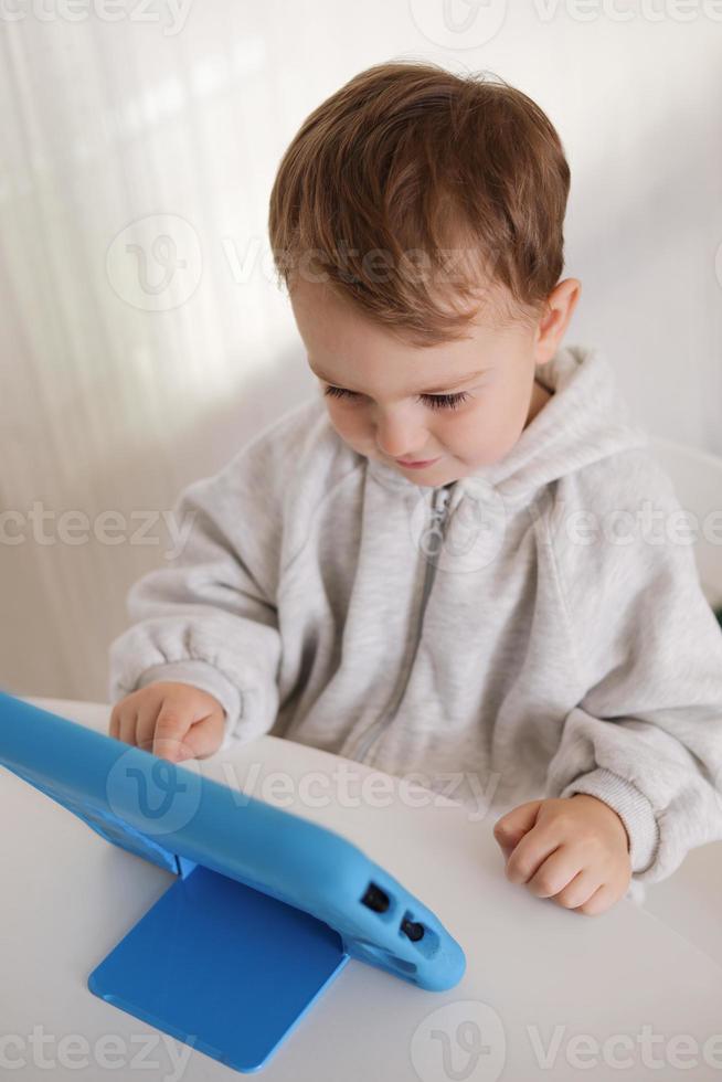 niño feliz jugando en la tableta digital en casa. retrato de un niño en casa viendo dibujos animados en la tableta. niño moderno y tecnología educativa. foto