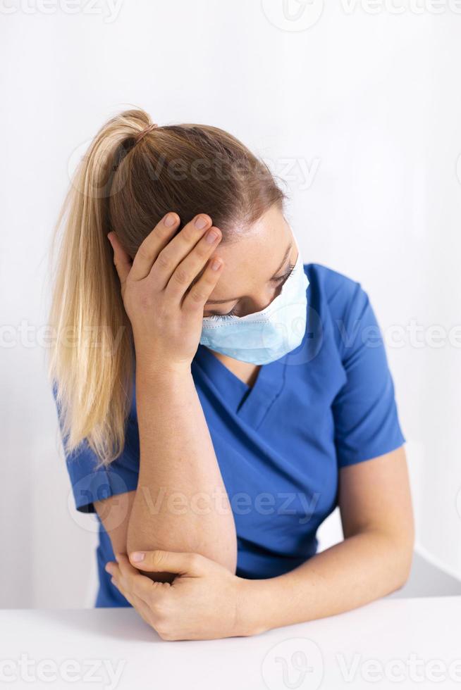Tired and exhausted nurse or doctor. Stressed female medical worker with protective face mask, depressed after working over hours due to coronavirus outbreak. Covid 19. Medicine, healthcare, pandemic photo