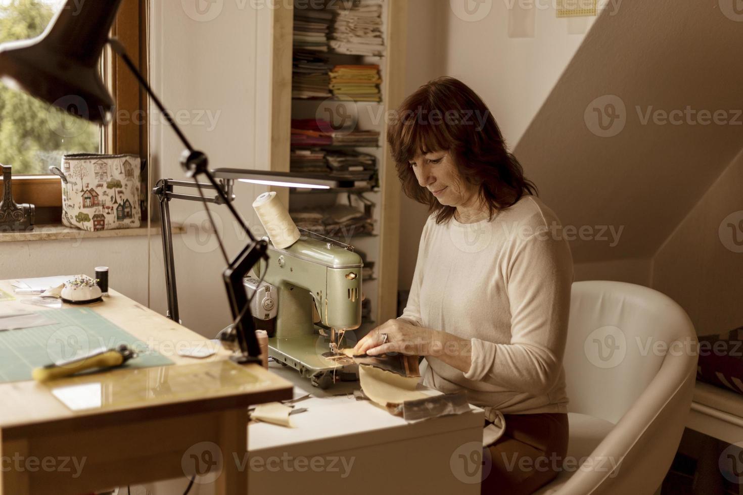 mujer morena caucásica cosiendo tela con una máquina de coser retro y vintage. moda, creación y sastrería. proceso de costura en atelier o taller. afición especial. interior acogedor y colores cálidos. foto