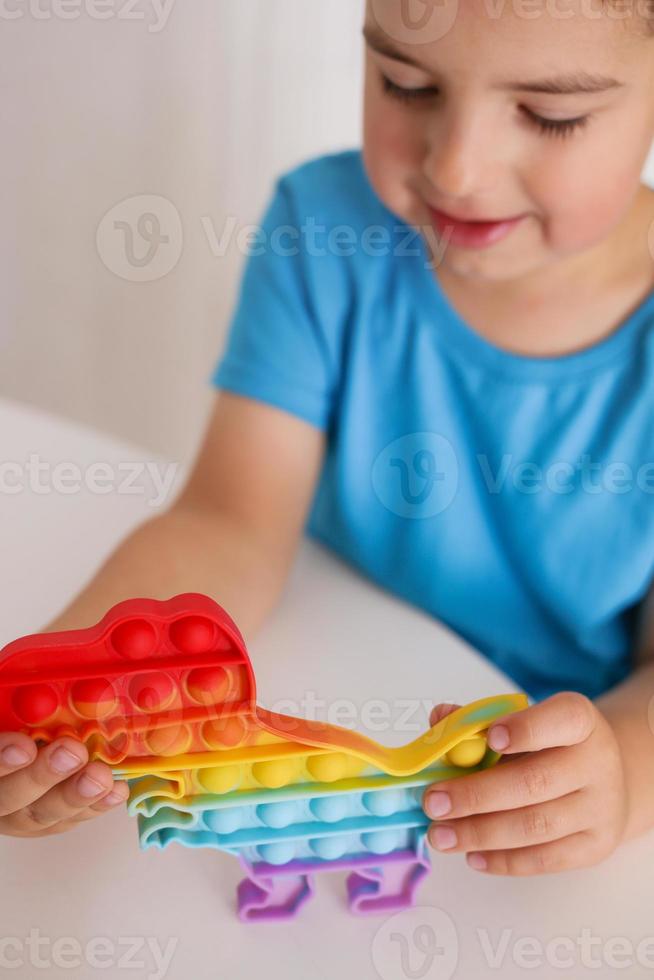Little boy plays with rainbow Pop it fidget toy. Antistress children game. Children's trendy silicone toys pop it to relieve stress and develop hand motor skills. Colorful hand toy with push bubbles. photo